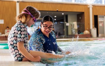 Swimming instructor helping child kick legs in water